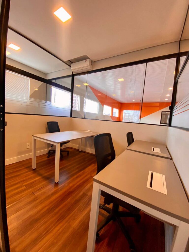 sala com 3 mesas e 3 cadeiras com cabeamento para utilização de notebook em um ambiente fechado com meia parede em vidro e privativo para trabalho ou estudo.